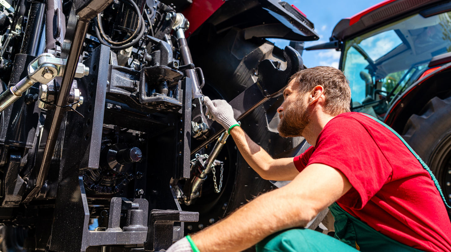 Agriculteur inspectant mécaniquement un tracteur d'occasion dans un atelier agricole, vérifiant l'état technique avant achat